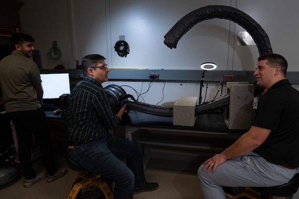 Ankush Dhawan, Chad Council, and Nathaniel Hanson in a dark lab test a vine robot, a 10-foot-long bendy tube.