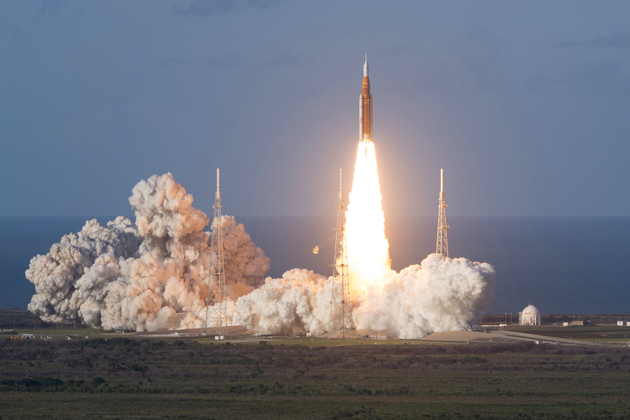 NASA's Space Launch System rocket lifts off from Kennedy Space Center, producing a massive plume of smoke and flame against an overcast sky during the Artemis I mission