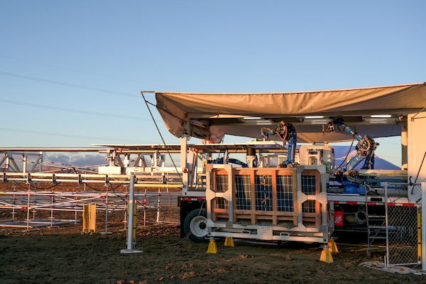 Robotic equipment on a truck at a solar farm, with metal frames and panels in the background under clear skies.