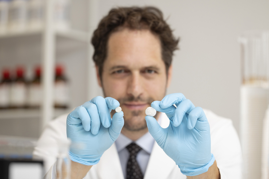 Aron Blaesi wears blue gloves while holding two spherical, lattice-like pills.