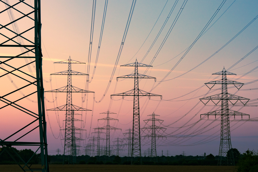 Rows of high‑voltage transmission towers and wires silhouetted against a colorful sunset sky.
