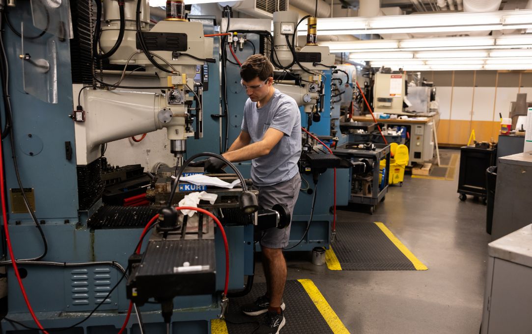 Person operating a milling machine in a workshop, surrounded by industrial equipment and tools.