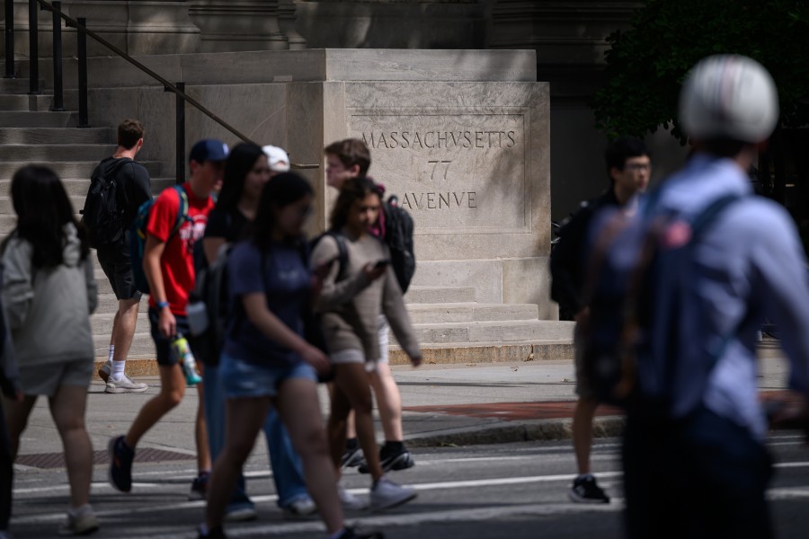 Students cross the street in front of the "77 Massachusetts Avenue" stone marker at the entrance to MIT.