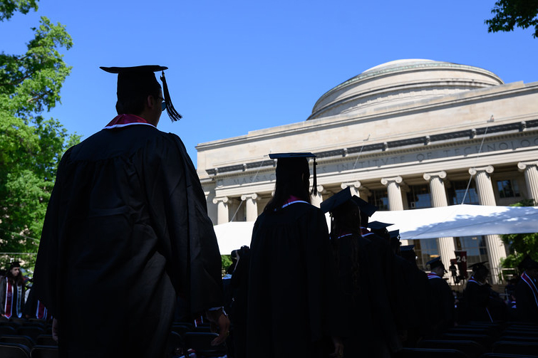 A group of graduates in black caps and gowns in front of MIT's Great Dome.