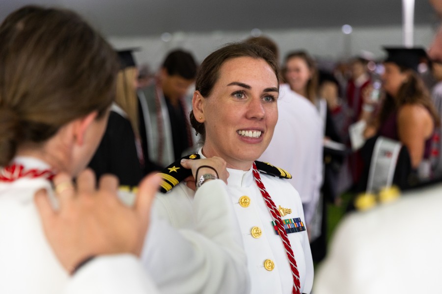 Woman in military dress uniform smiles while being congratulated during a graduation ceremony, surrounded by people in academic regalia.