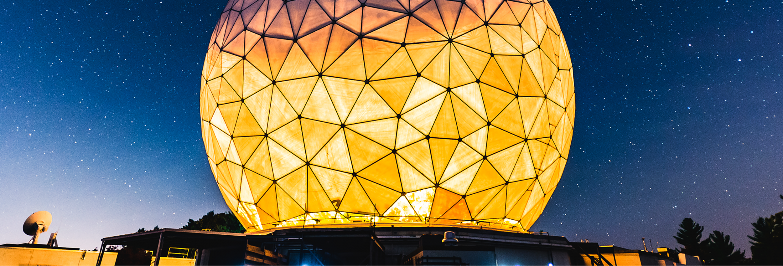 The large radome covering the Haystack Ultrawideband Satellite Imaging Radar is lit from within, glowing yellow against a starry night sky.